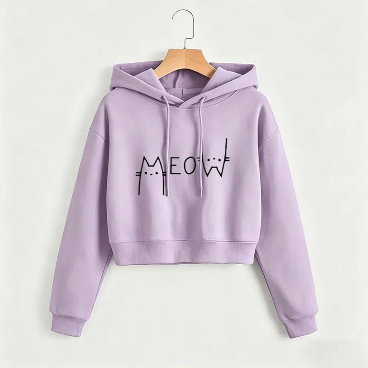 Lilac cropped Meow hoodie on a wooden hanger against a light wall, with a black cat print, hood, drawstrings and long sleeves
