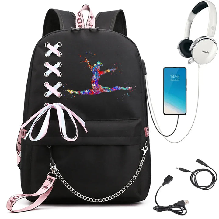 Black backpack featuring a bright split-leap gymnast print, ribbon crosses, pink webbing and chain, beside electronics props.