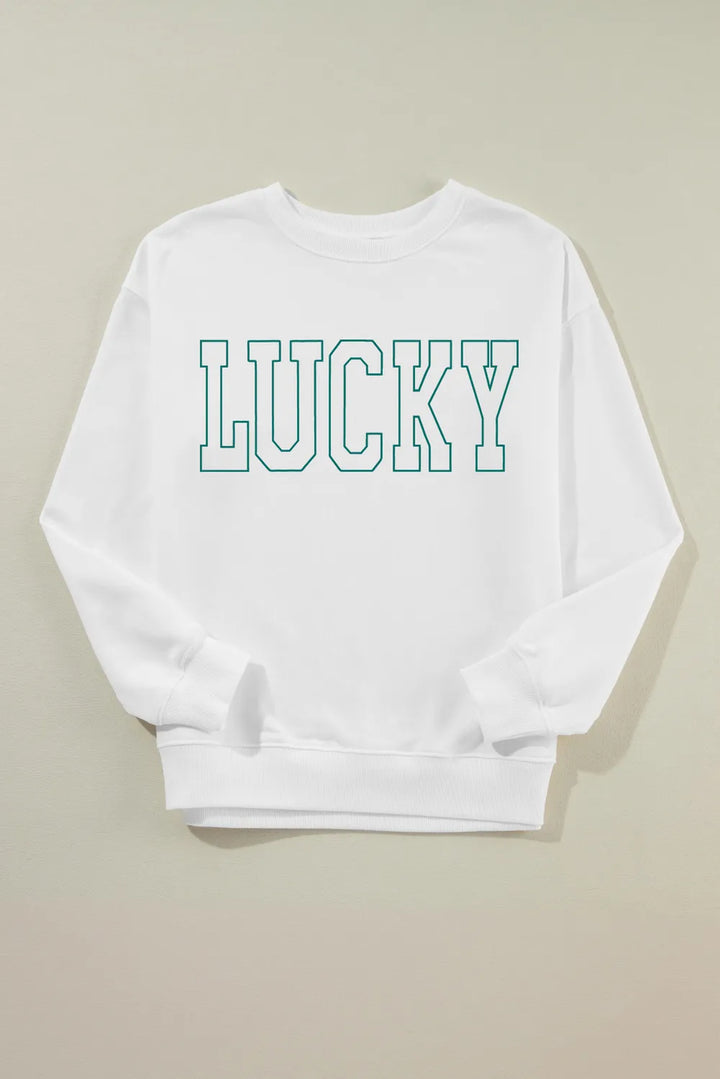 “Smiling woman in LUCKY graphic sweatshirt sitting on a bench with autumn leaves around”

