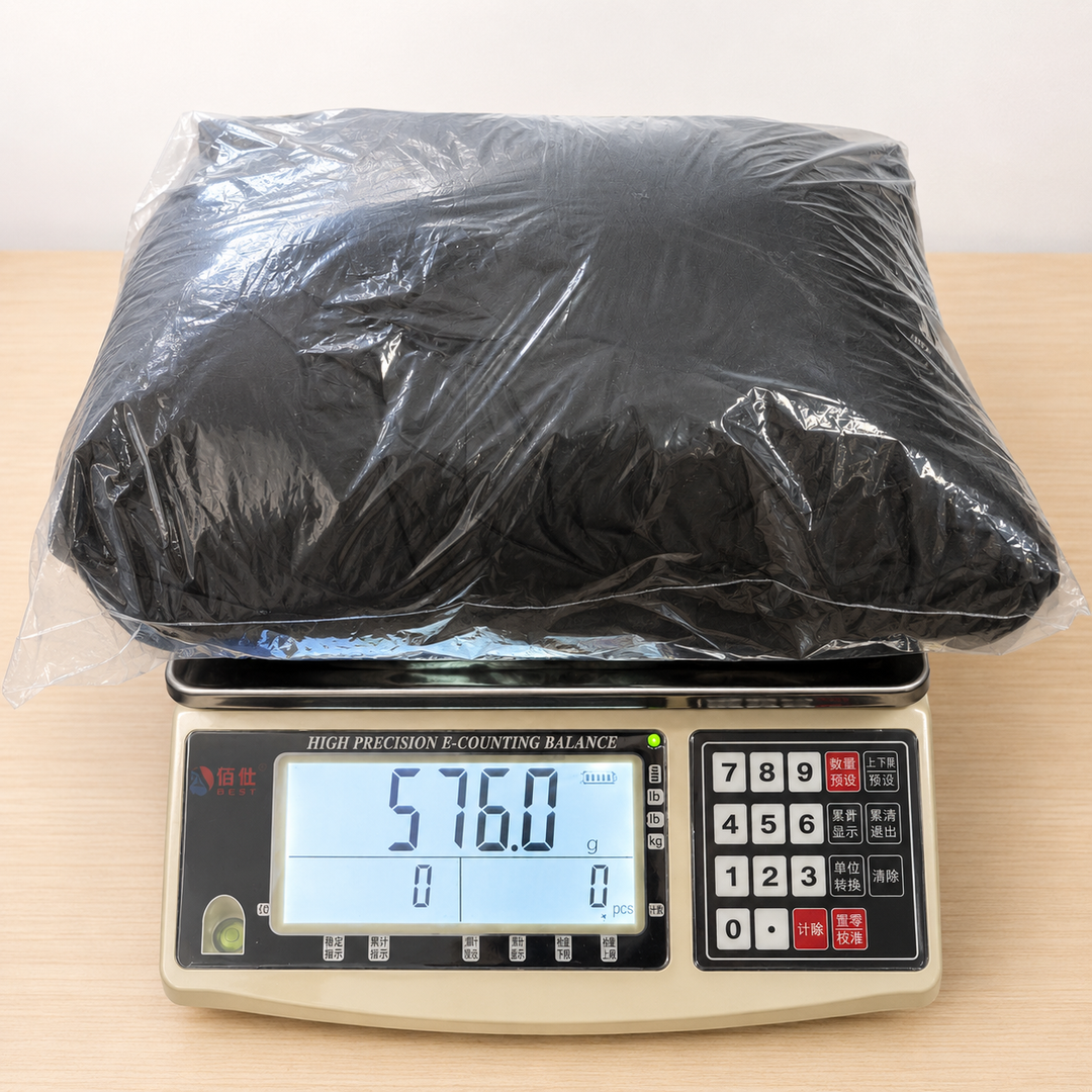 Digital scale with a large black object wrapped in plastic on a light wooden surface