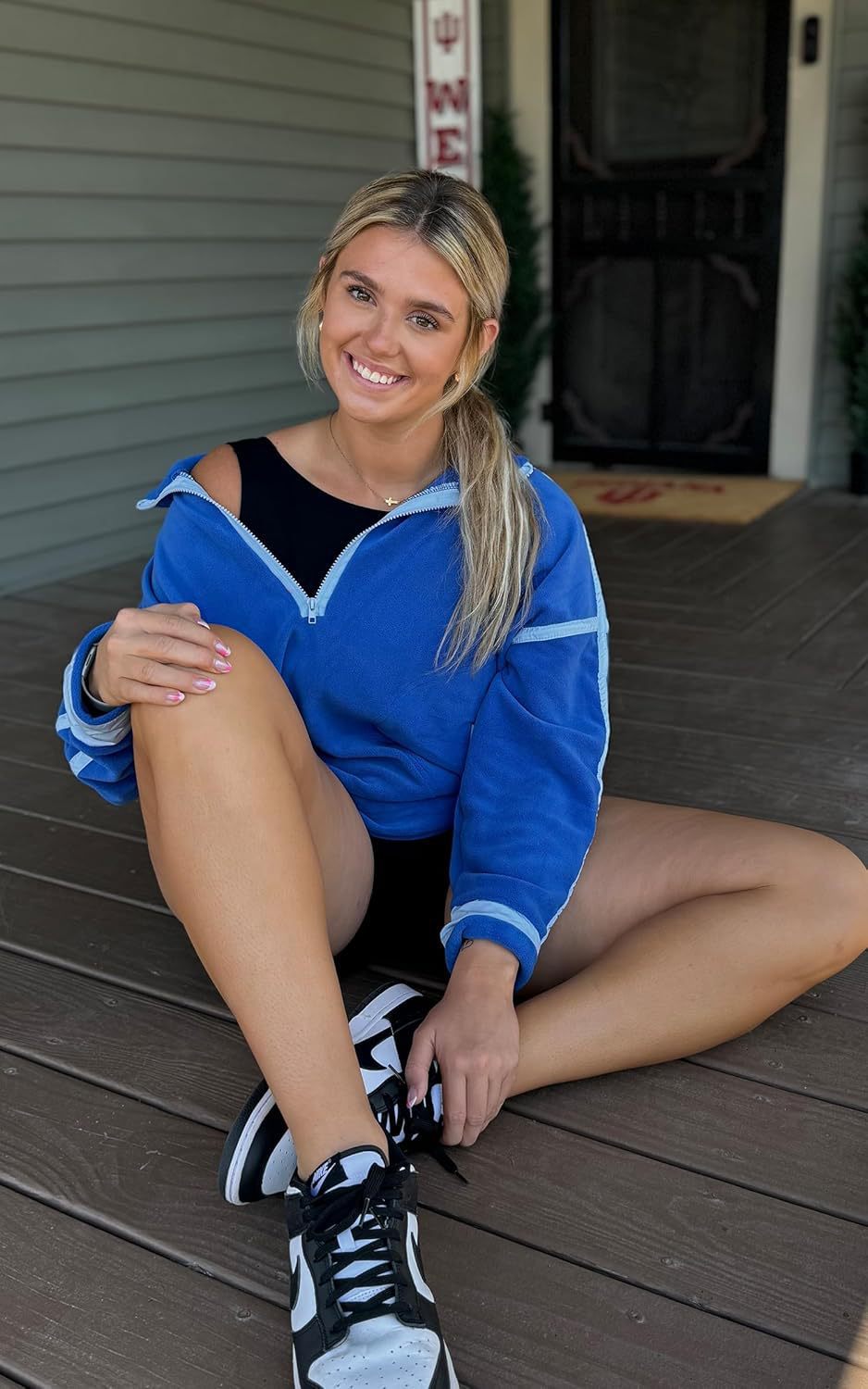 Woman in blue jacket and black sneakers sitting on a wooden deck.