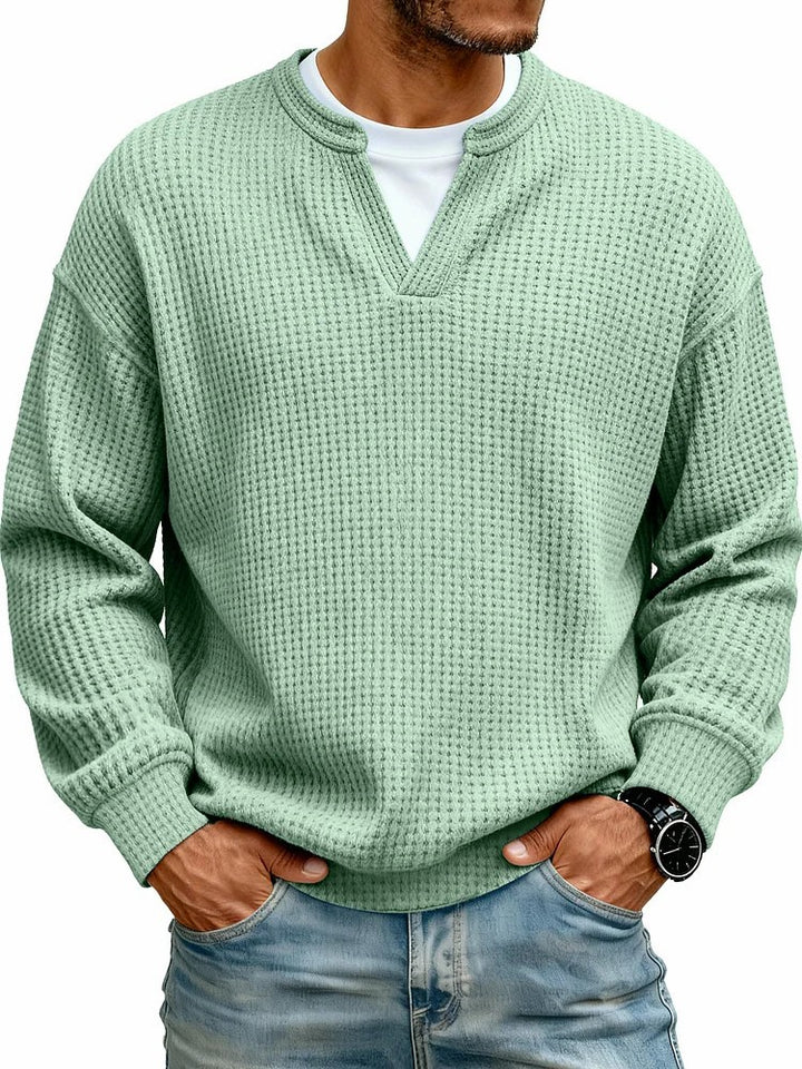Person wearing a green textured sweater and blue jeans on a white background