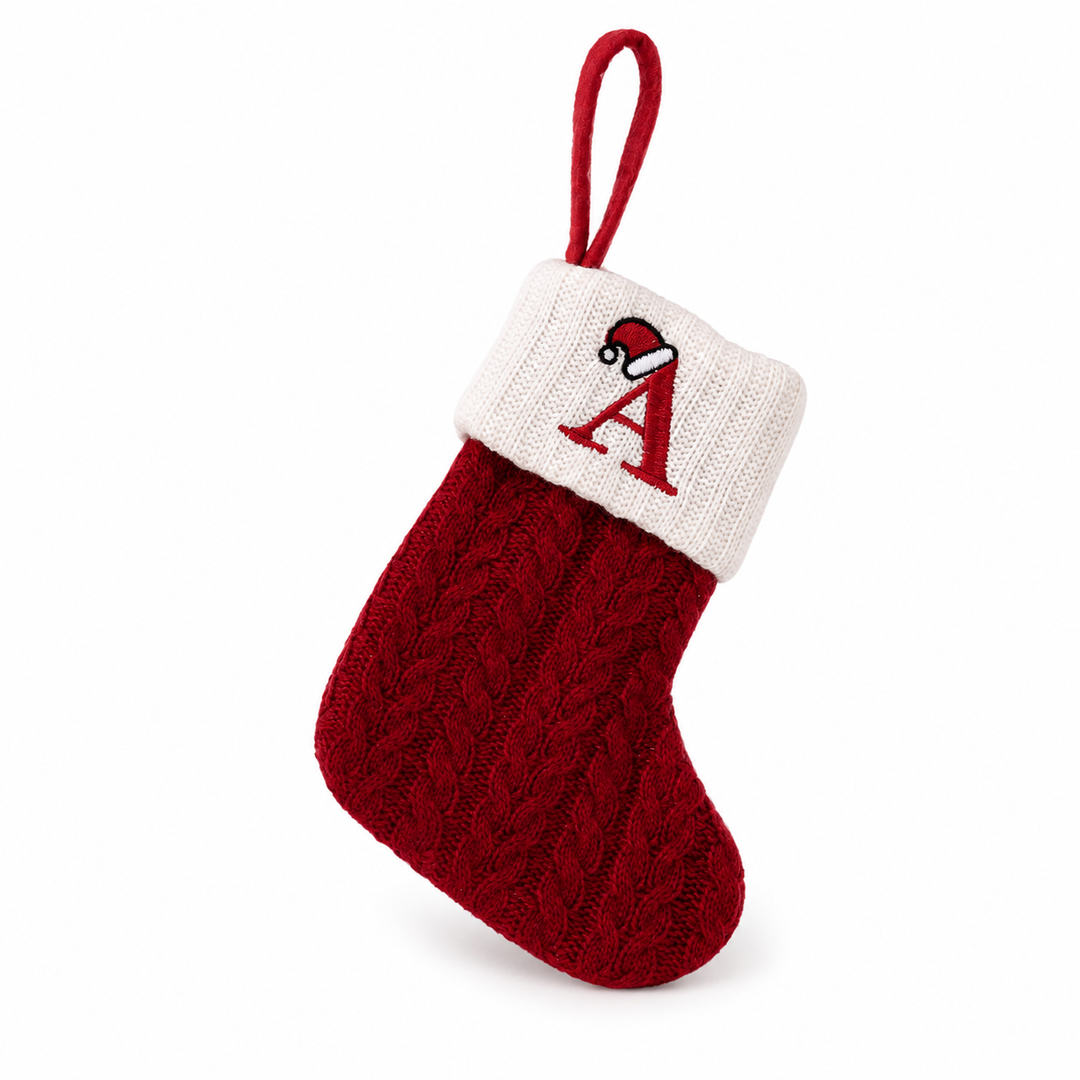 Cable-knit Christmas stocking in red with ivory contrast cuff, letter A embroidery, Santa hat detail, and a red hanging loop.