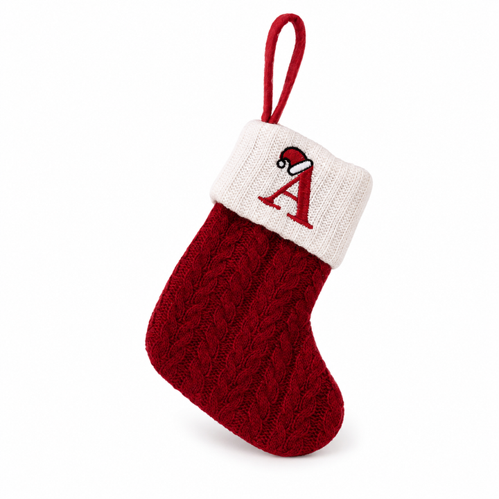 Cable-knit Christmas stocking in red with ivory contrast cuff, letter A embroidery, Santa hat detail, and a red hanging loop.