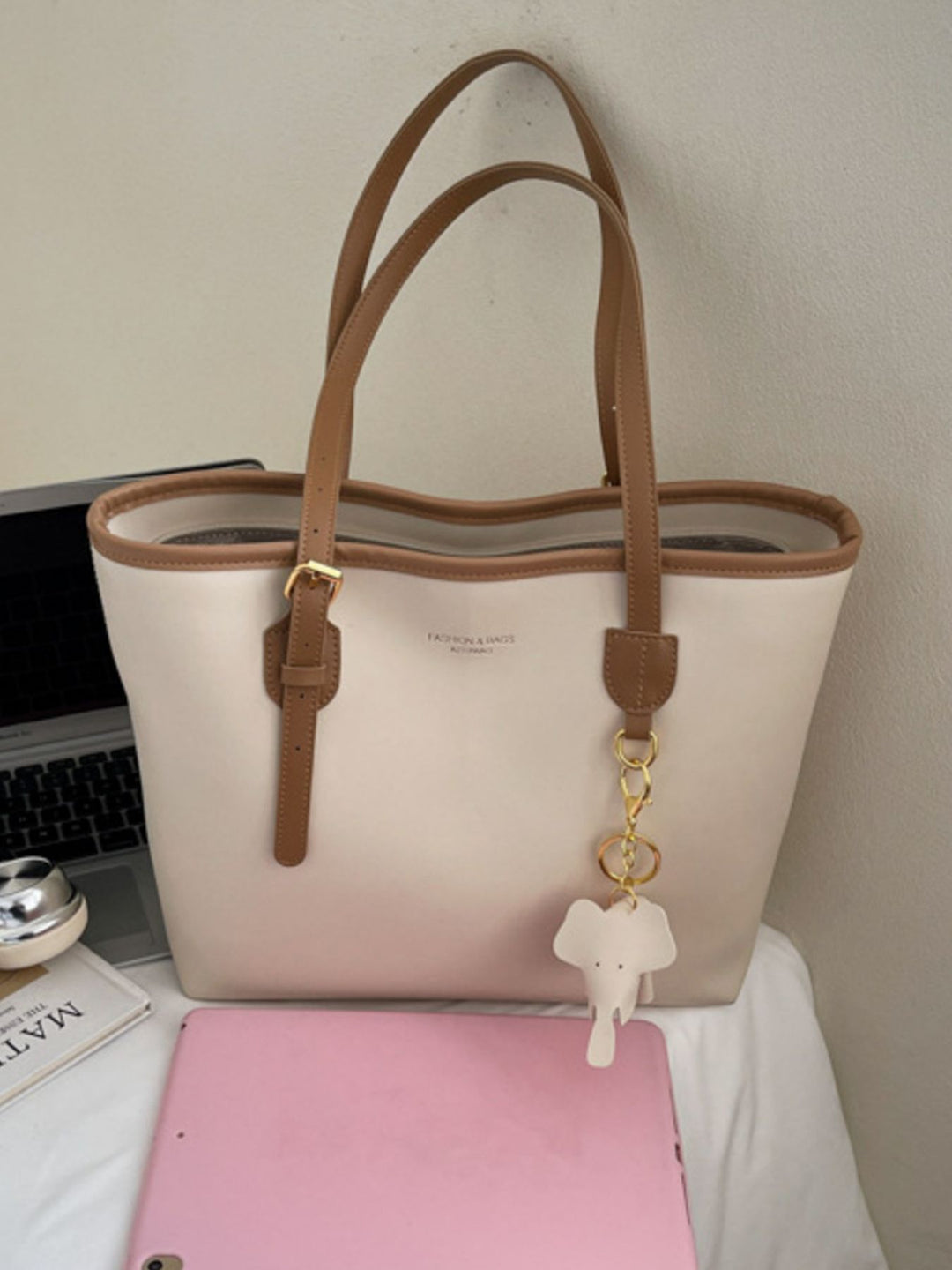 Beige tote bag with brown handles on a desk with a pink tablet and laptop.