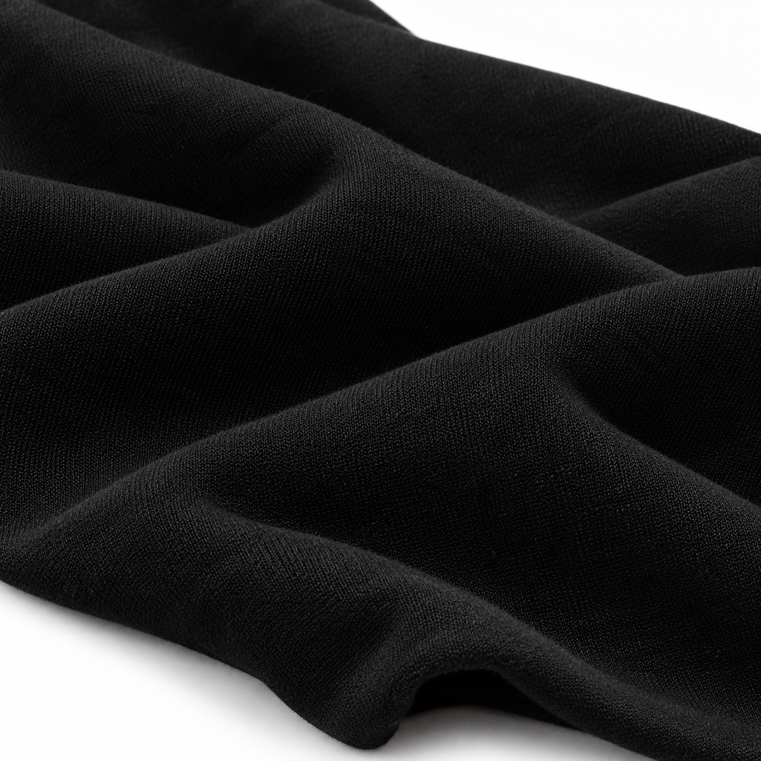 Close-up of black hoodie fabric arranged in soft folds, showing its visible surface texture against a clean white background.