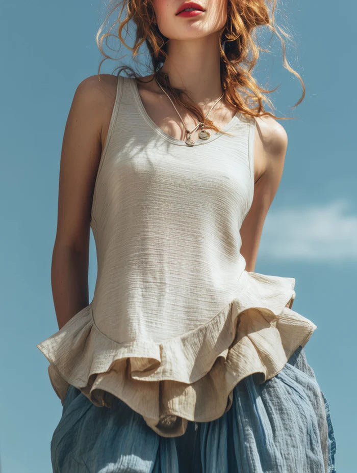 Woman wearing a beige top with ruffled layers against a blue sky.