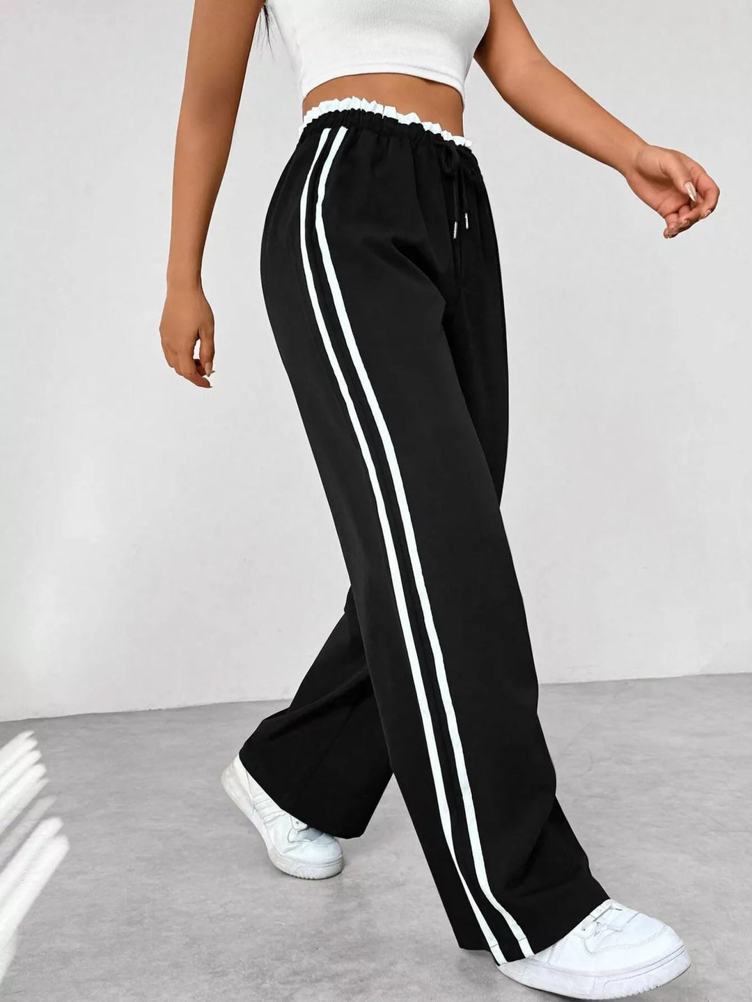 Navy blue track pants with white stripes worn by a person on a light gray floor.