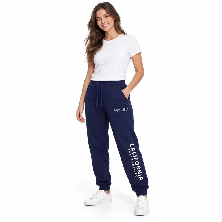 Navy blue California sweatpants worn by a female model in a white T-shirt and white sneakers, in a full-length view on white.