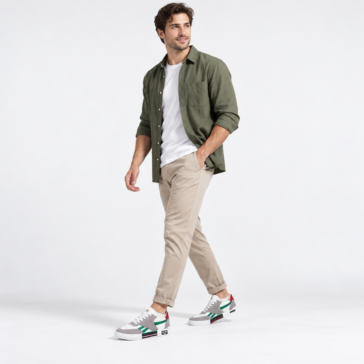 Male model wearing green striped canvas shoes with gray overlays, white laces and red heel tab in a clean studio.