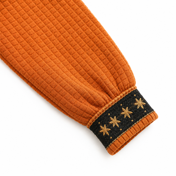 Detailed orange sweater sleeve and black cuff with gold star accents, highlighting texture, ribbing and decorative stitching.