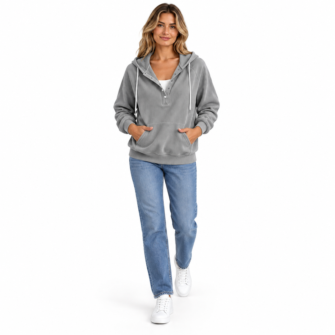 Adult woman wearing a grey hooded pullover with blue jeans and white sneakers, shown walking against white studio background.