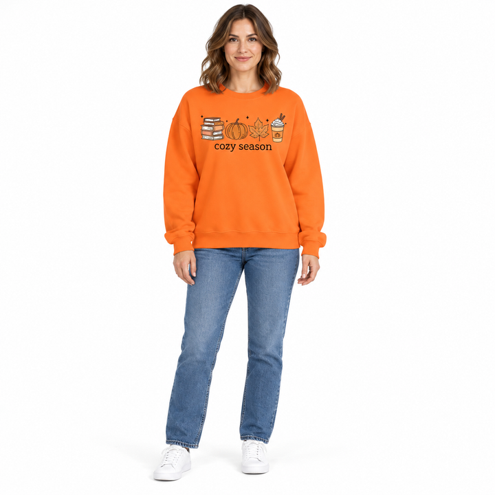 Orange crewneck sweatshirt on a full-length woman with denim jeans, showing the cozy season print against the white backdrop.