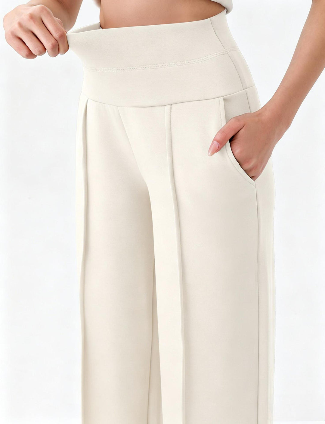 Supplier close-up of white yoga trousers, showing the broad waistband being stretched, curved pocket opening and front pleat.