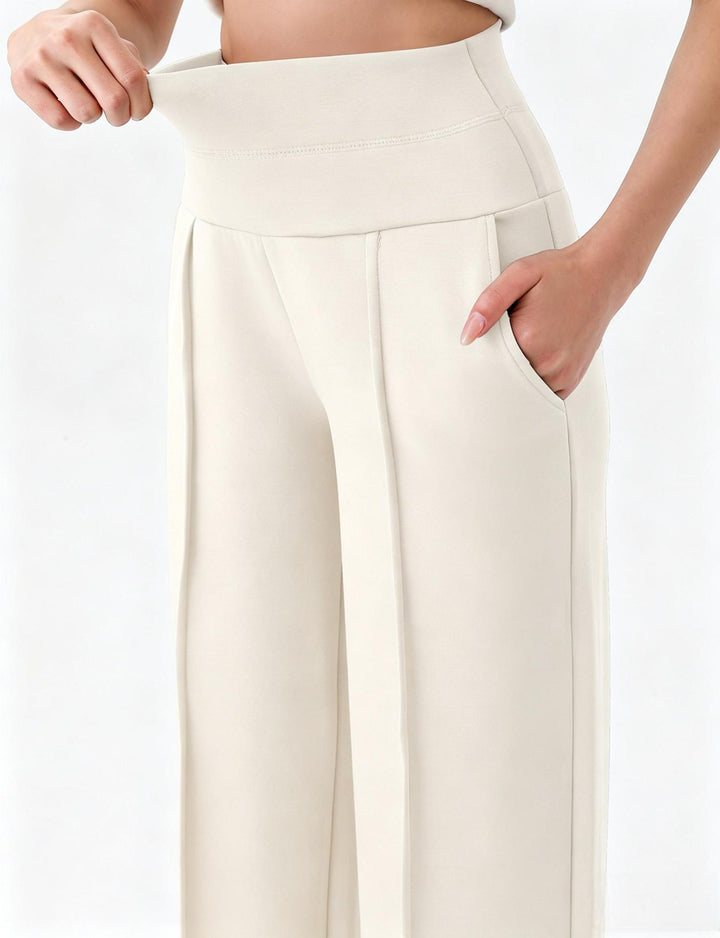 Supplier close-up of white yoga trousers, showing the broad waistband being stretched, curved pocket opening and front pleat.