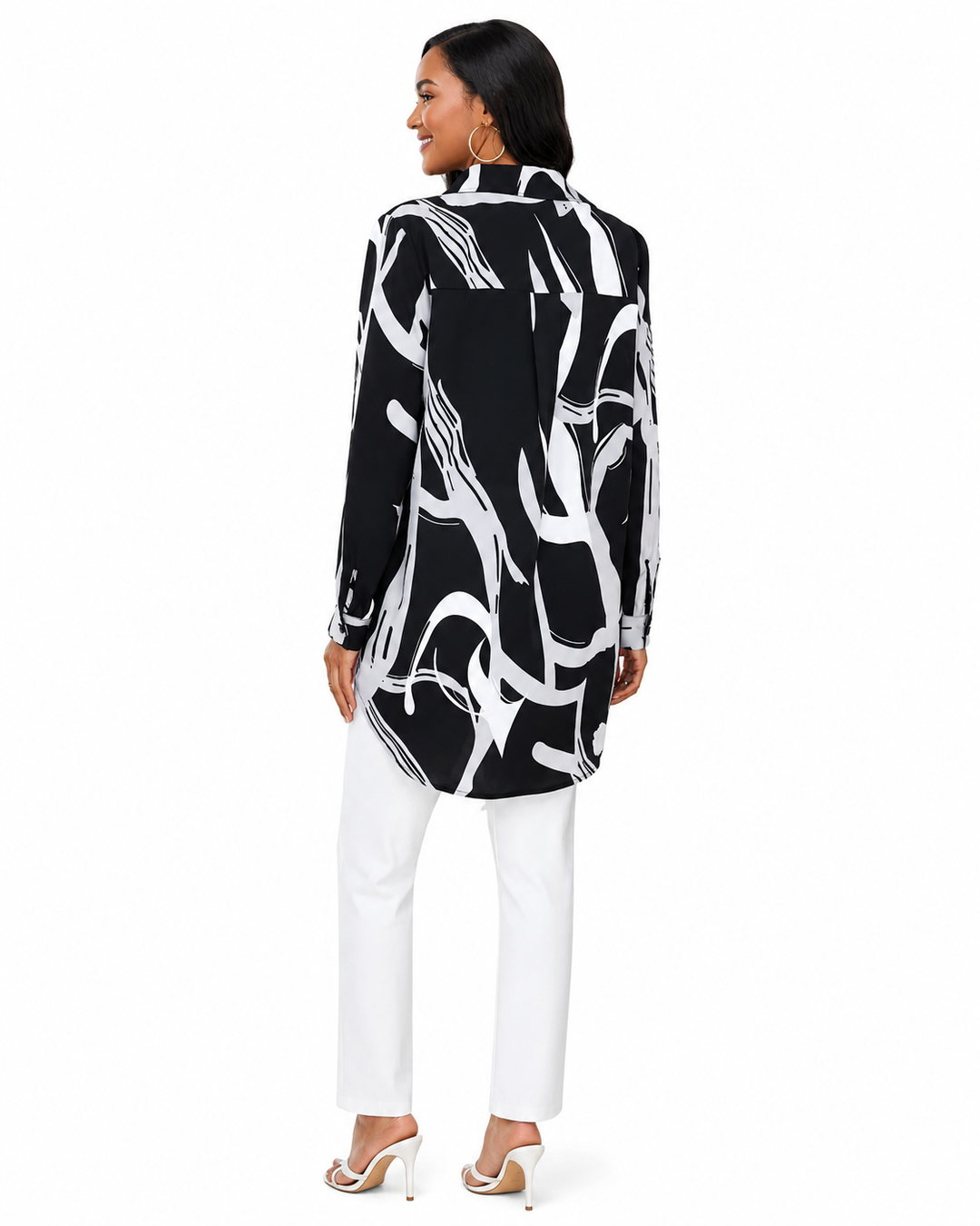 A woman shown from the back wearing a black long-sleeve tunic top with a bold white abstract brushstroke pattern, paired with white pants and white high-heeled sandals, against a plain white background.