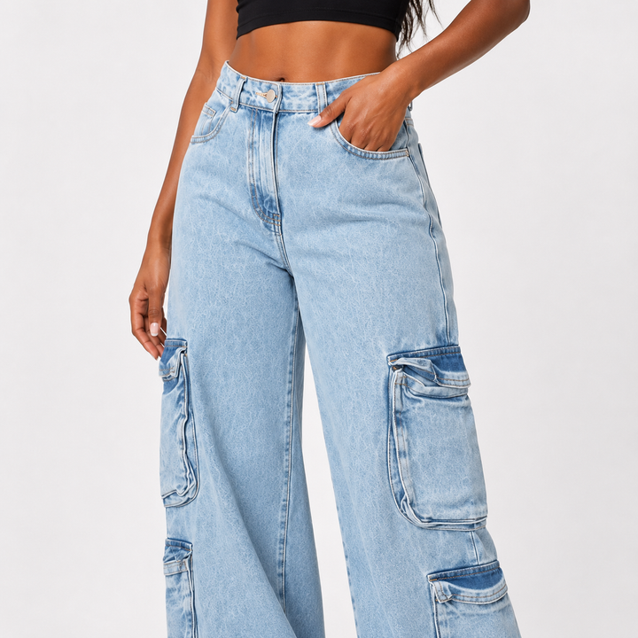 A model wearing light-wash wide-leg cargo jeans with large patch pockets, paired with a black crop top against a plain light gray studio background.