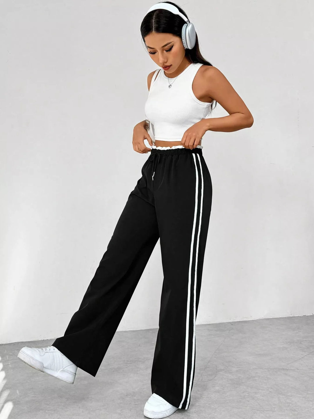 Woman wearing a white crop top and black high-waisted pants with white stripes, standing against a plain background.