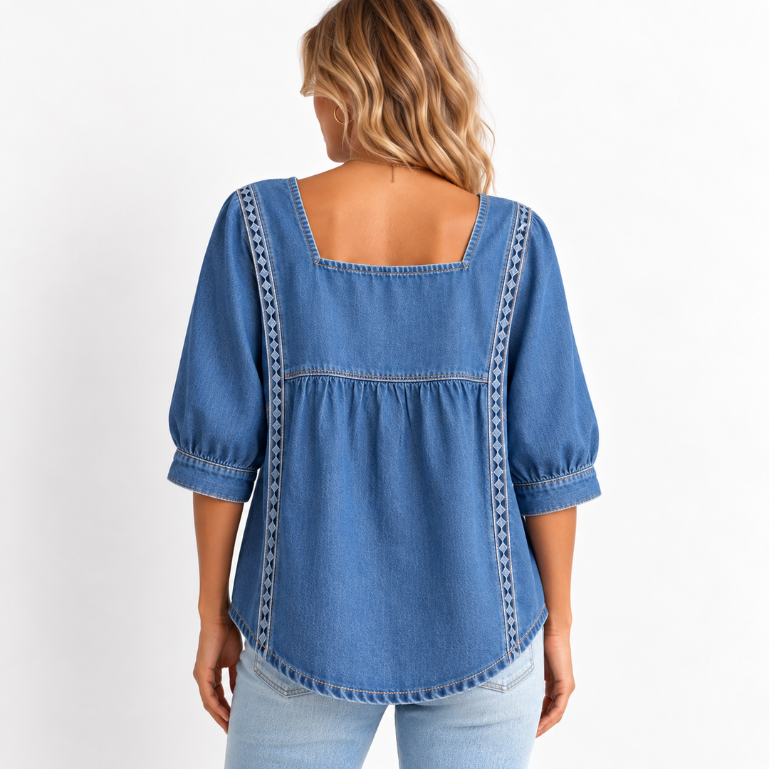 Back view of the denim blouse on a model showing the square back neckline, gathered seam and lace patchwork trim.