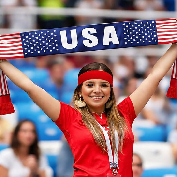 Woman in red shirt and headband holding a USA flag scarf in a stadium setting