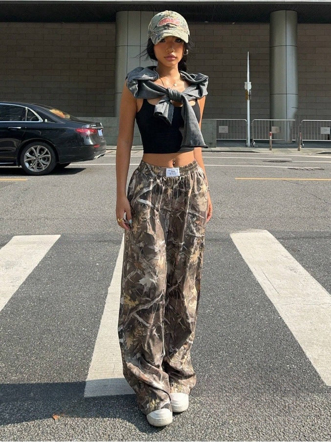 Person wearing a black top and camouflage pants standing on a street.
