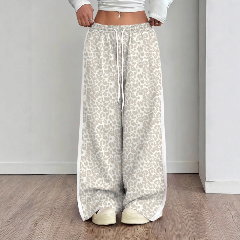 Person wearing light-colored leopard print pants with a white top and shoes on a wooden floor.