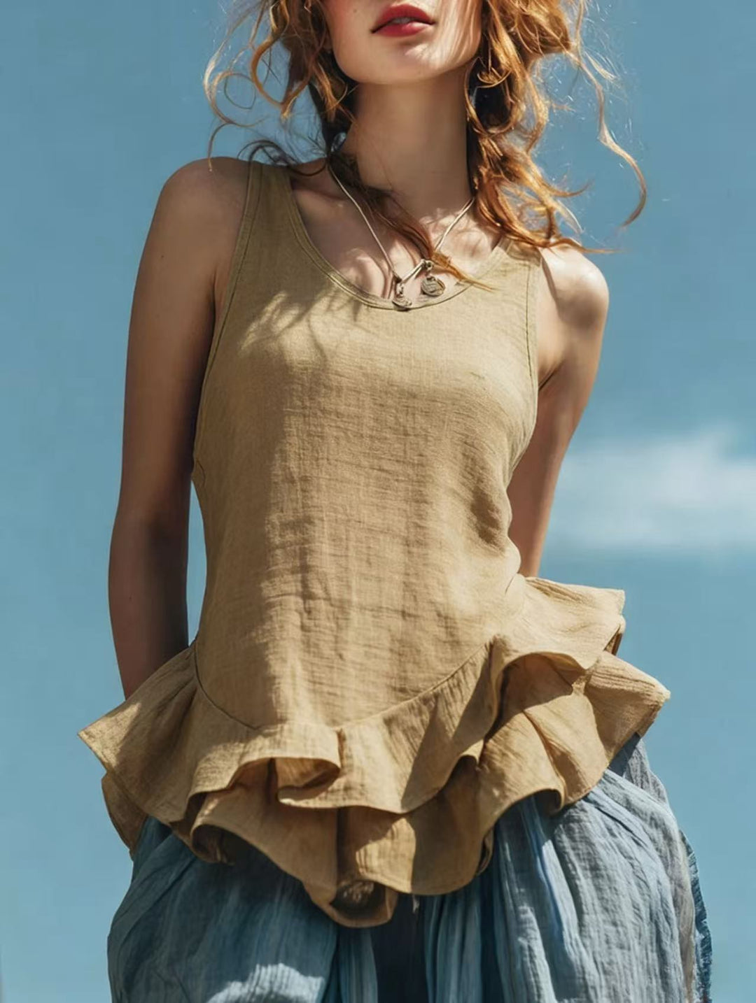 Woman wearing a beige sleeveless top with ruffled layers against a blue sky.