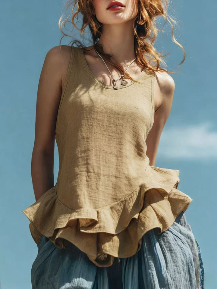 Woman wearing a beige sleeveless top with ruffled layers against a blue sky.