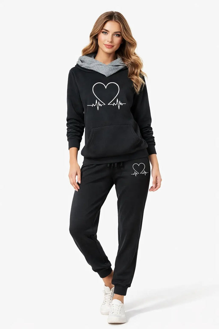 women's love heart printed sports suit lifestyle shot model sitting comfortably in living room wearing black hooded top and pants for quiet luxury casual moments