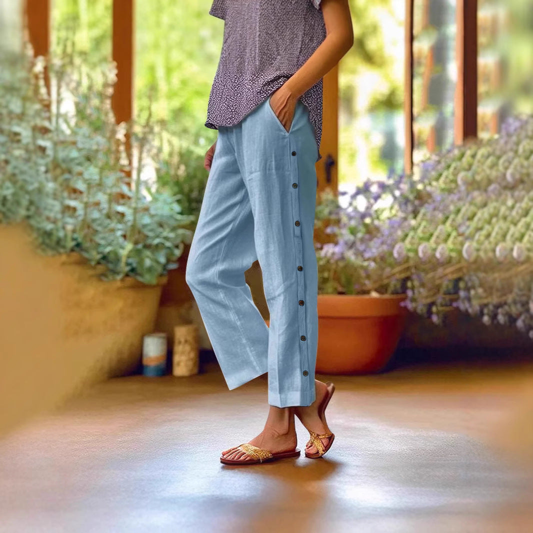 Person wearing light blue pants with buttons, standing indoors with plants in the background
