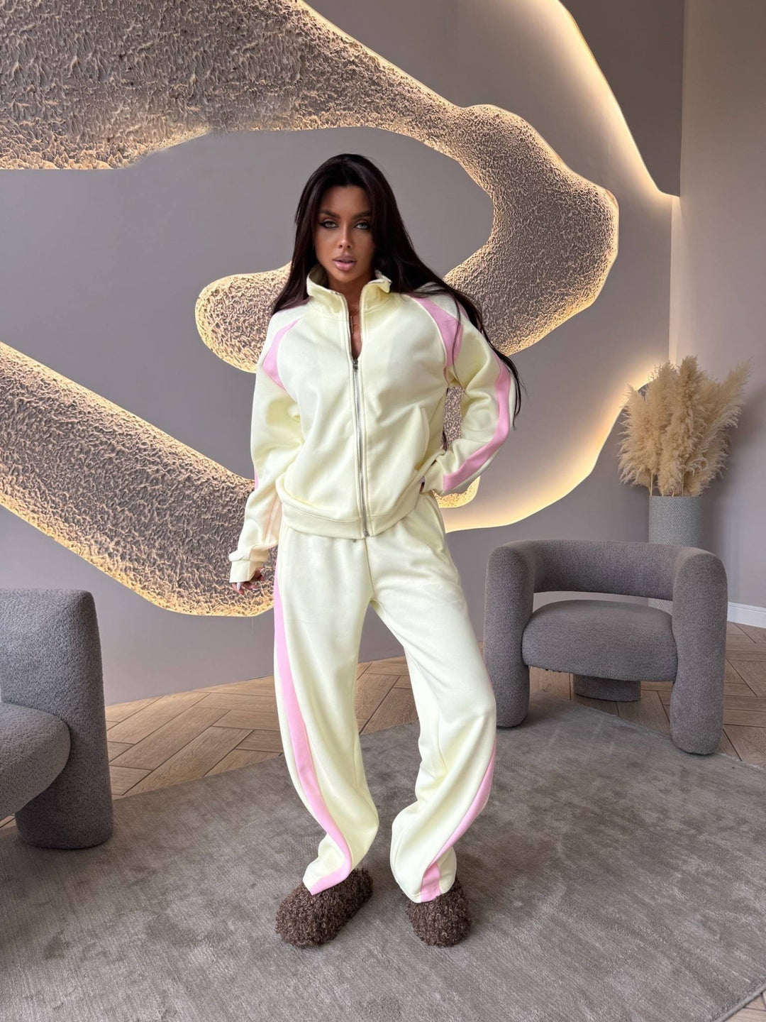 Person wearing a light-colored tracksuit with pink accents in a modern room.