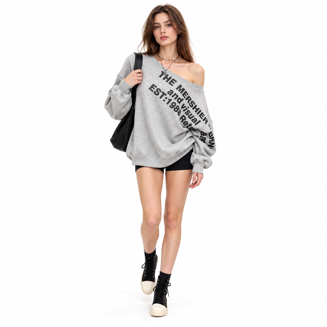 Model walks in a grey printed pullover with a black shoulder bag, black shorts and high-top shoes on a white studio backdrop.