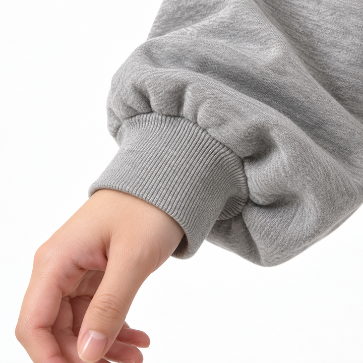 Close-up of the grey ribbed cuff and sleeve on a model, showing a cuff edge, gathered fabric and folds on a white background.