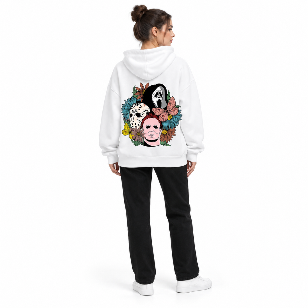 Full-body rear view of a woman wearing the white hooded pullover with floral mask back print, black trousers and white shoes.