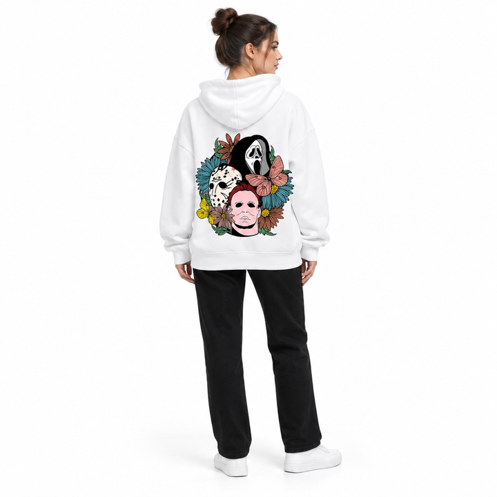 Full-body rear view of a woman wearing the white hooded pullover with floral mask back print, black trousers and white shoes.