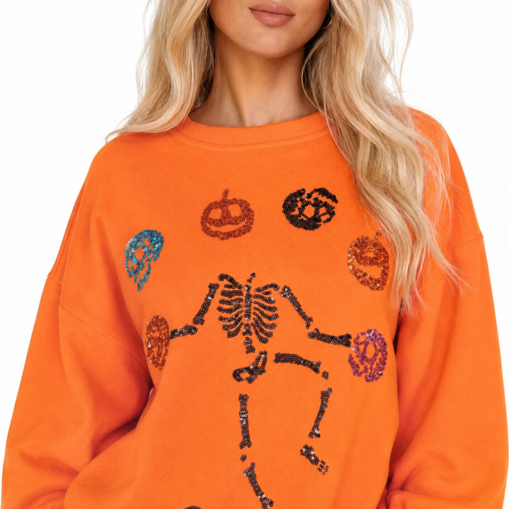 Close-up of orange sweatshirt showing skeleton pumpkin sequin detail, crew neckline and cotton polyester fabric blend clearly
