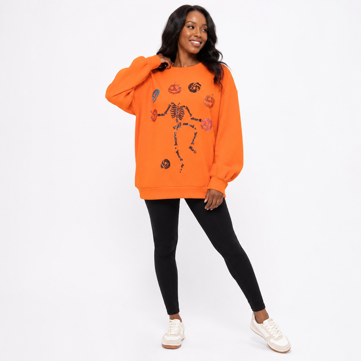 Orange Halloween sweatshirt front view with skeleton pumpkin sequin motif and long sleeves, photographed on a clean backdrop.