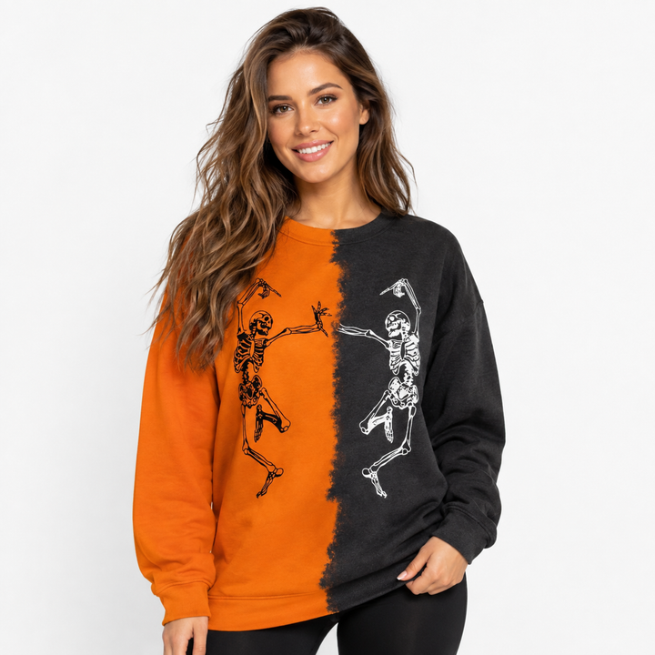 Woman wearing orange and black Halloween skeleton sweatshirt with dancing skeleton print on a clean white studio background.
