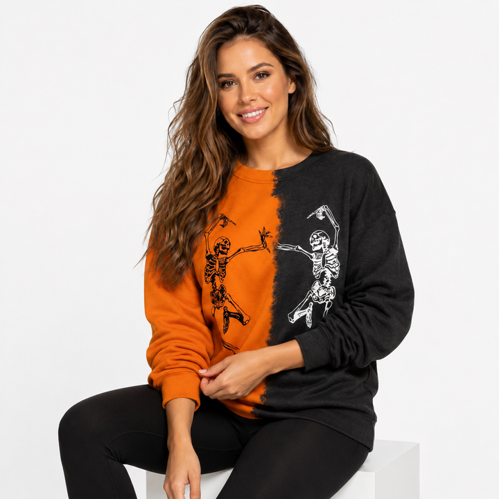 Woman seated in orange and black Halloween skeleton sweatshirt with dancing skeleton print on a clean white studio background.