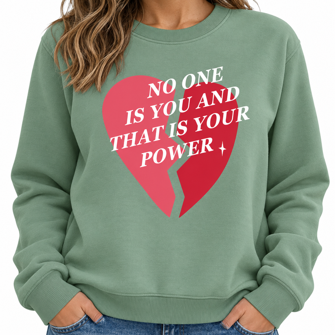 Close-up of the olive green sweatshirt front showing the split pink and red heart graphic, white lettering and crew neckline.