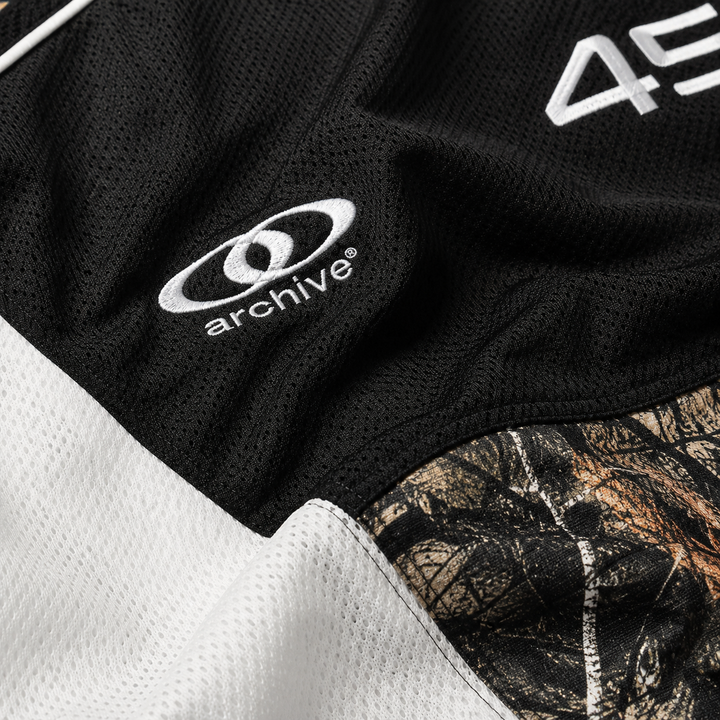Macro view of black mesh hoodie fabric with white panel, camouflage insert, stitching and archive embroidery in close detail.