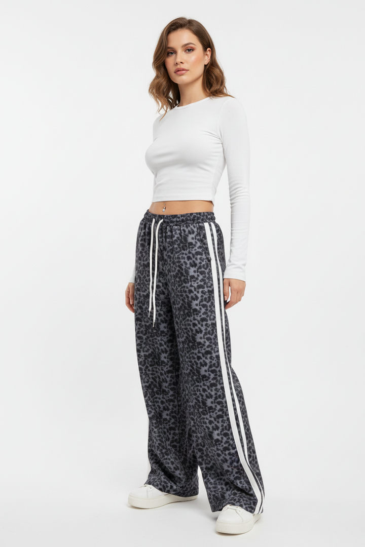 Woman wearing a white long-sleeve top and leopard print pants with white stripes on a white background