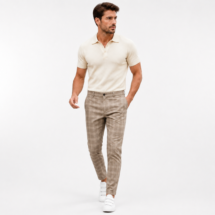 Khaki plaid trousers on an adult male model in a clean bright white studio walking pose with a cream polo and white sneakers.