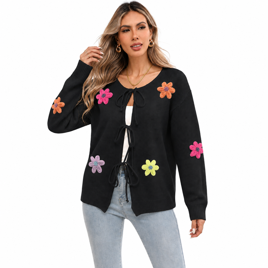 Black floral tie-front knit cardigan on a woman with visible face, colorful flower appliques and front bow details on white.