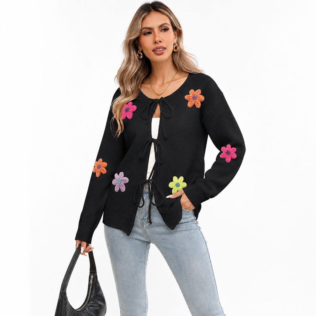 Black floral tie-front knit cardigan on a woman with visible face, light-wash jeans, colorful flower appliques and black handbag.