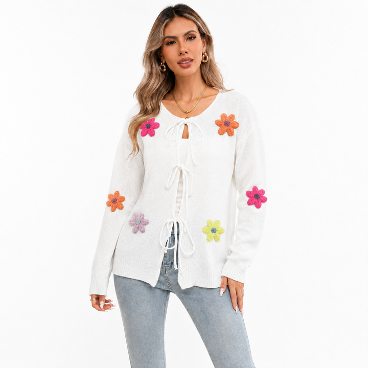 White floral tie-front knit cardigan on a woman with visible face, front bow closures, long sleeves and colorful flower appliques.