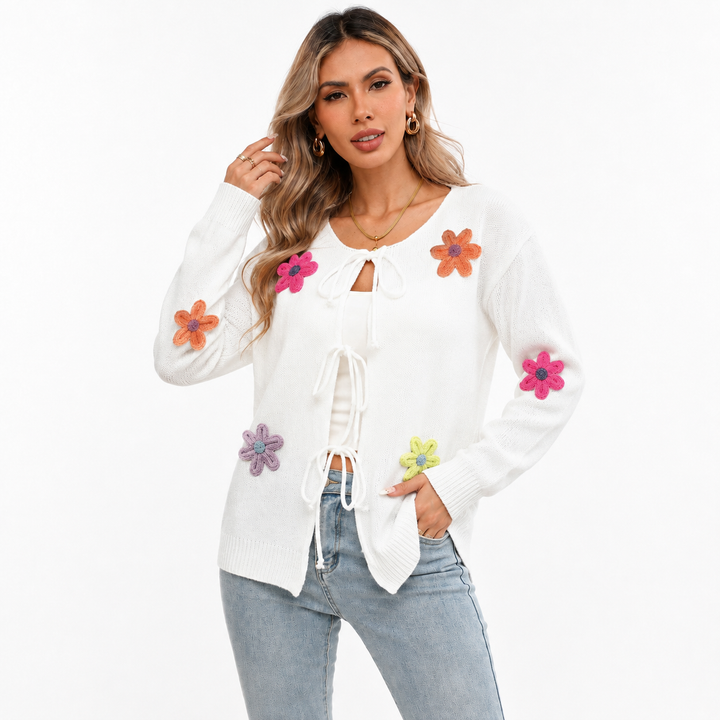 White floral tie-front knit cardigan on a woman with visible face, colorful flower appliques, long sleeves and light-wash jeans.