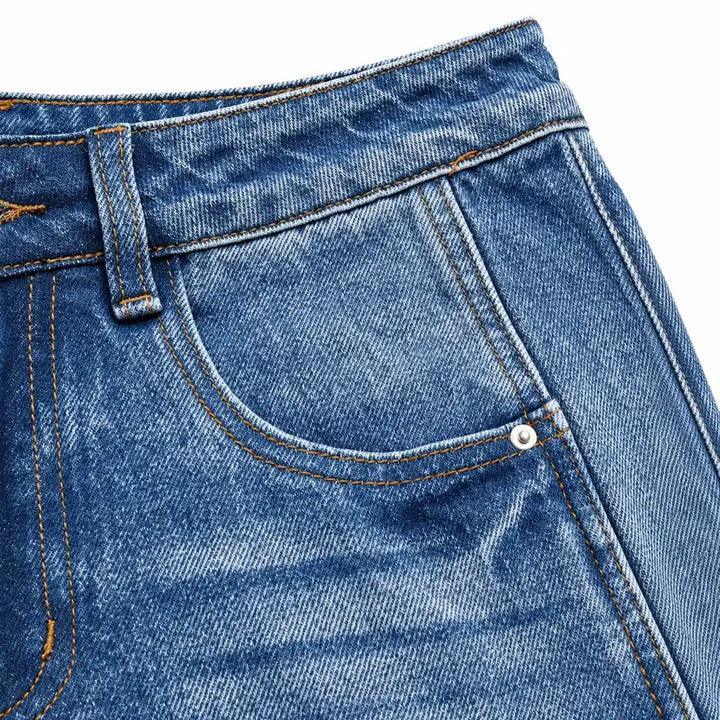 Close-up of the curved front pocket on washed jeans, showing the silver rivet, belt loop, contrast stitching and denim weave.