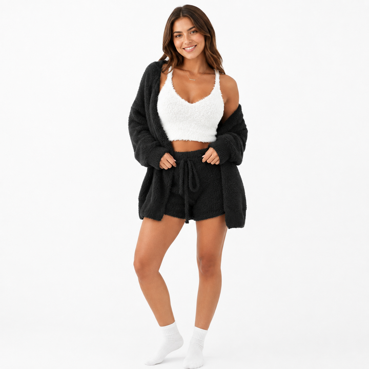 Black fuzzy open cardigan and drawstring shorts with white cropped top shown on a female model in a clean white studio scene.