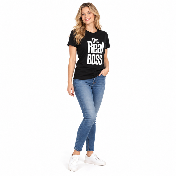 Full-body blonde adult woman wearing a black The Real Boss printed tee with jeans and white sneakers in a white studio scene.